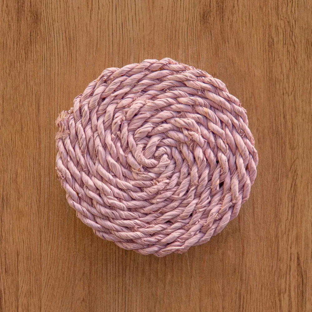 Pink woven coaster on a wooden surface.