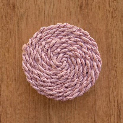 Pink woven coaster on a wooden surface.