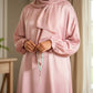 Person wearing a pink dress holding a rosary in a softly lit room.