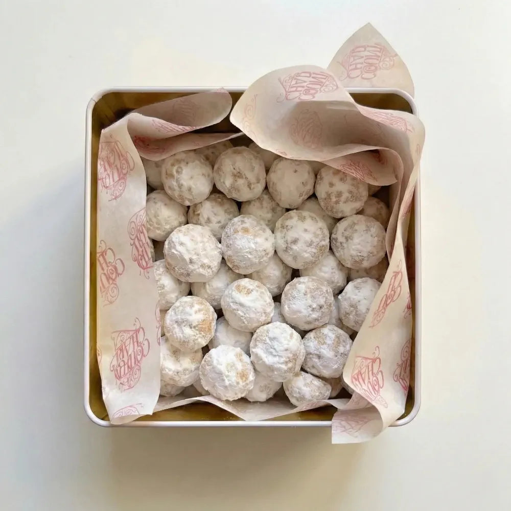 Box of powdered sugar-coated cookies with branded paper on a light background