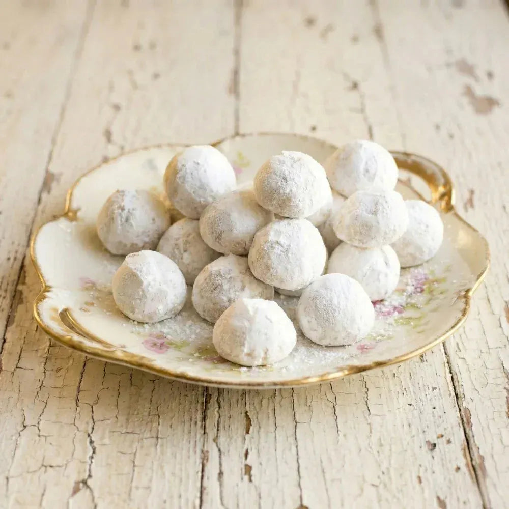 Powdered sugar-coated kahk treats on a decorative plate with a rustic wooden background