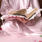 Women wearing pink polka dot satin isdal reading Holy book sitting on the prayer rug