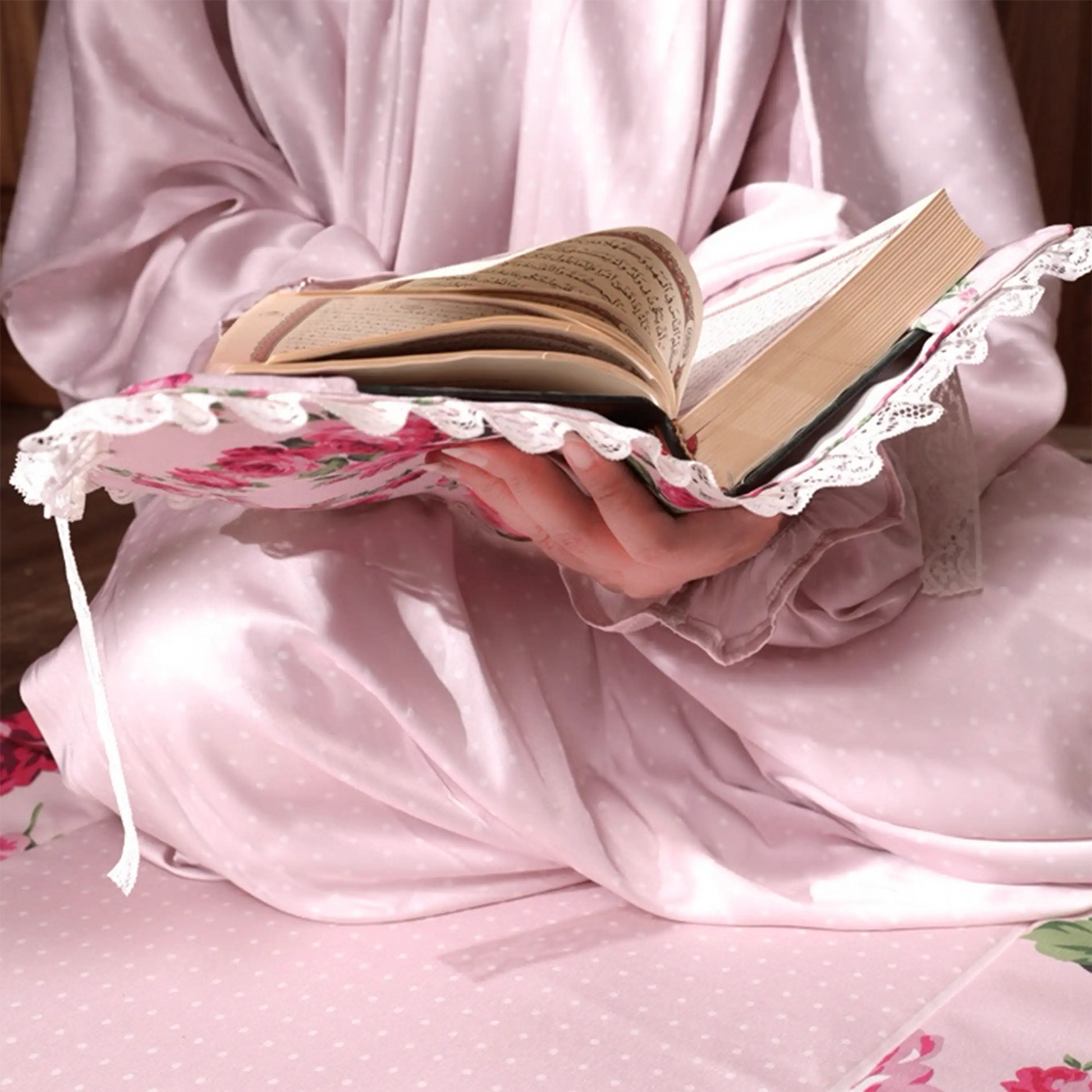 Women wearing pink polka dot satin isdal reading Holy book sitting on the prayer rug