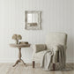 Cozy living room with armchair, side table, and decorative mirror on a white paneled wall.