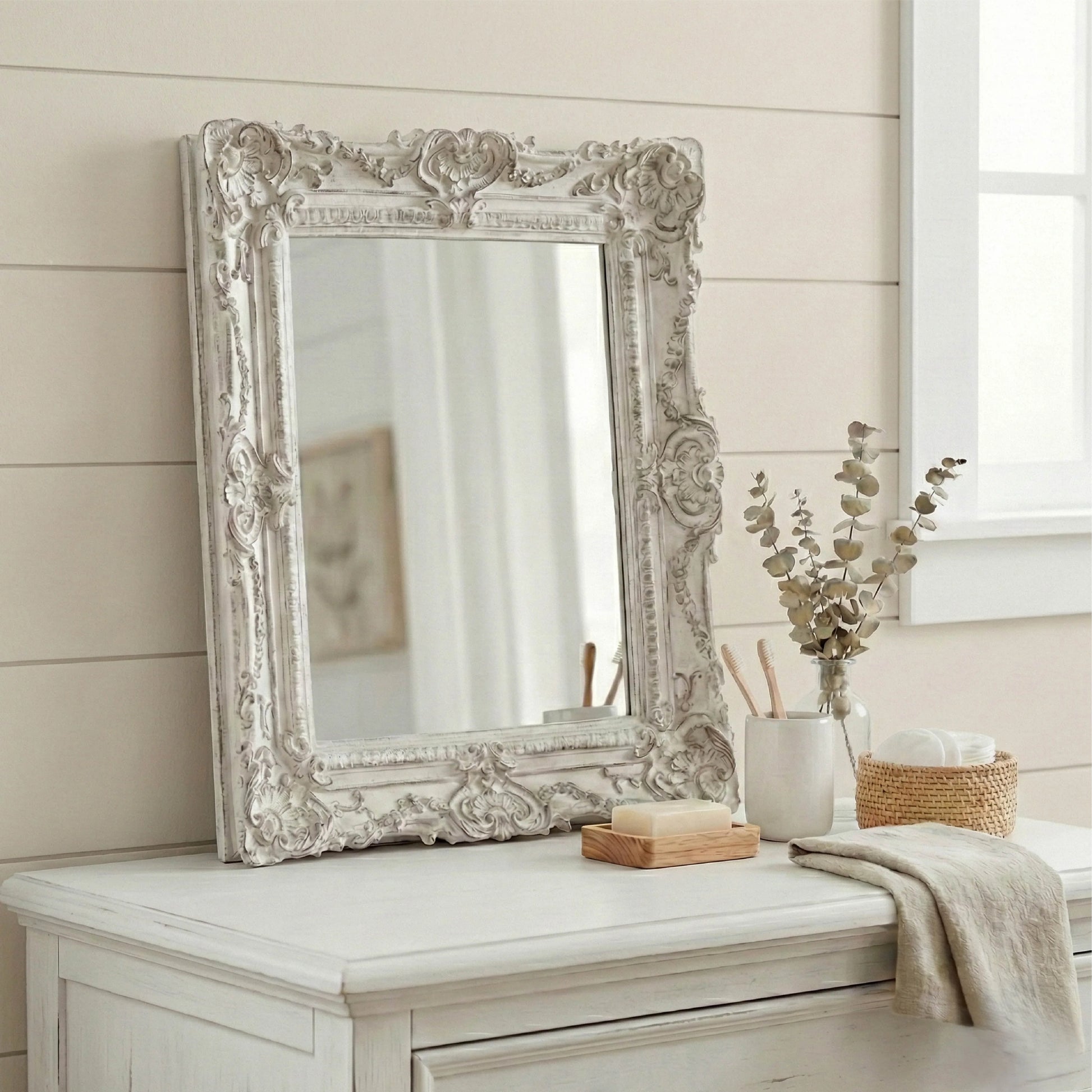 Decorative mirror with ornate frame on a white dresser against a neutral wall.