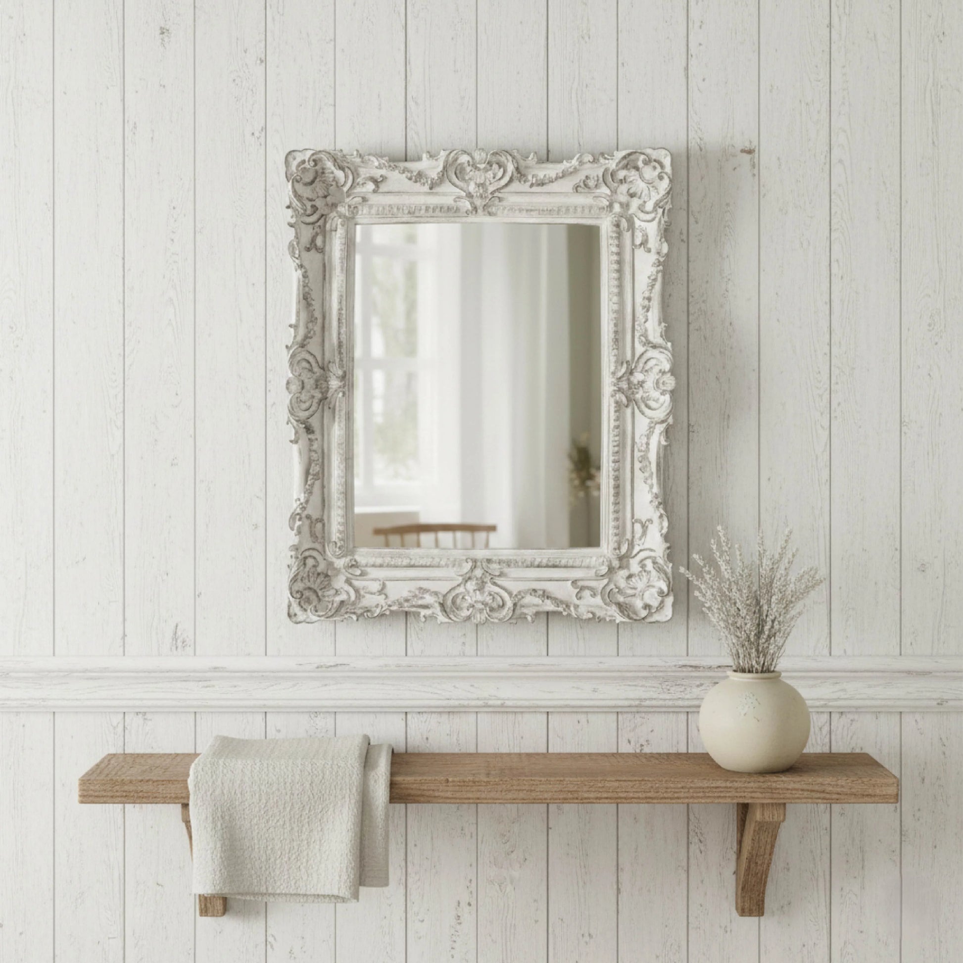Decorative mirror with ornate frame above a wooden shelf on a white paneled wall.