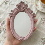 Pretty Shabby Wall Mirror – Oval Fleur held by hand above a floral tablecloth