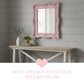 Pink ornate mirror above a wooden table with decorative items on a gray paneled wall.