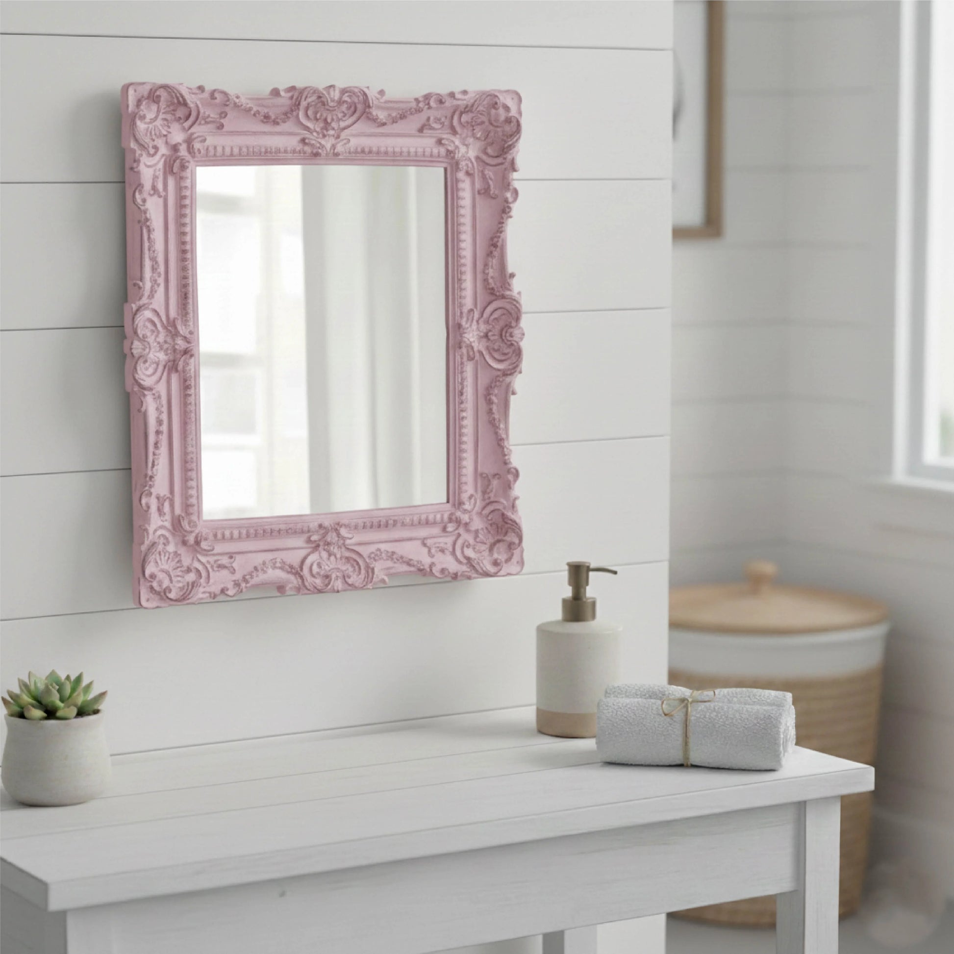 Decorative pink mirror on a white wall above a white surface with bathroom items.