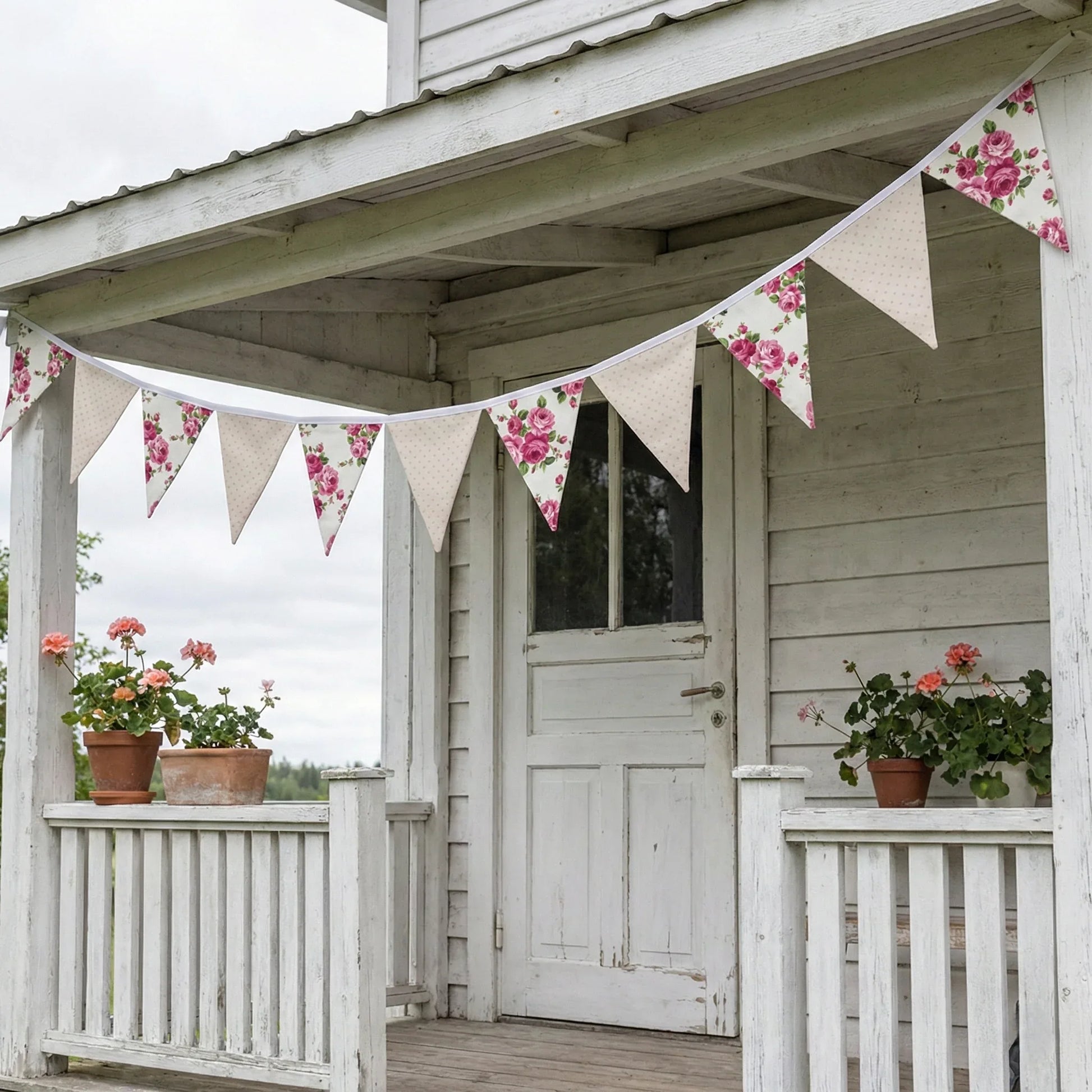 Floral and beige bunting on a wooden porch with potted plants.