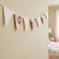 Floral fabric bunting hanging on a beige wall with a bedroom in the background.