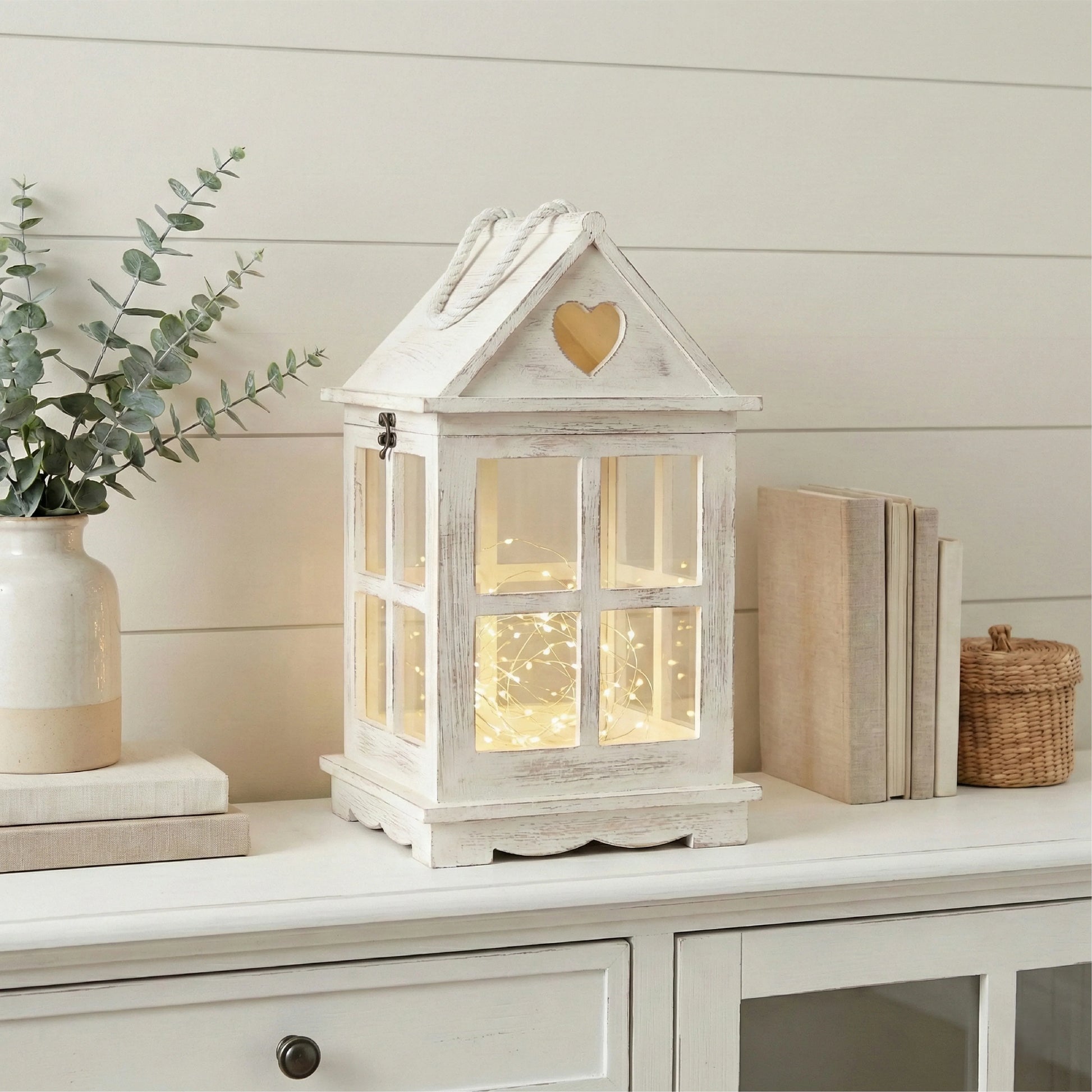 White decorative lantern with heart design on a shelf with books and plants