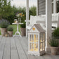 Decorative lantern with fairy lights on a wooden deck with potted plants and a white chair in the background.