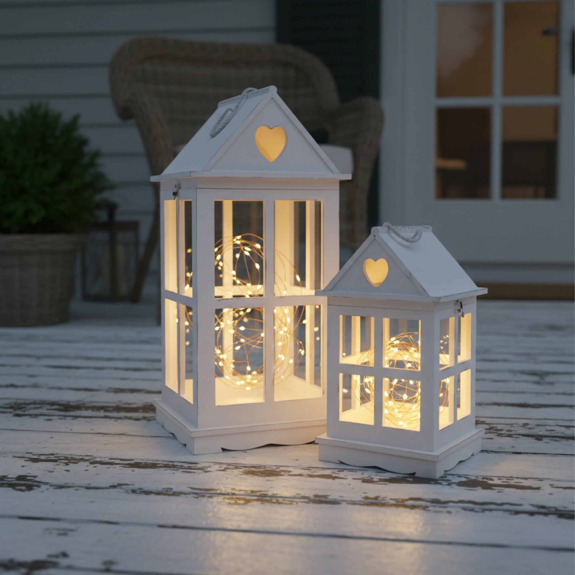 Two illuminated white lanterns with heart designs on a wooden surface.