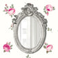 Ornate vintage oval mirror with floral frame against white background with pink rose patterns