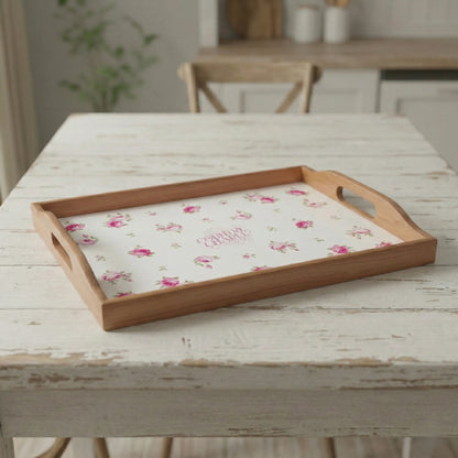 Wooden serving tray with a pink floral pattern on a white base, resting on a distressed white wooden table.