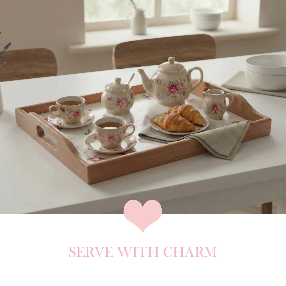 Wooden floral tray with a tea set, croissants, and cream pitcher on a white table, featuring a pink heart below.