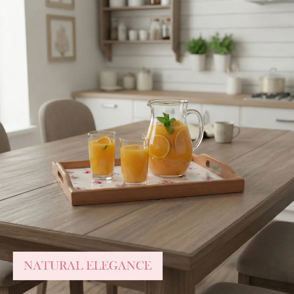 Wooden floral tray with a glass pitcher of orange juice and two glasses on a wood table in a white kitchen.