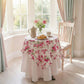 Round table with floral tablecloth in a bright room with large windows and curtains.