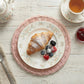 Round Wicker Placemat with breakfast setting featuring croissant, berries, tea, and floral plate