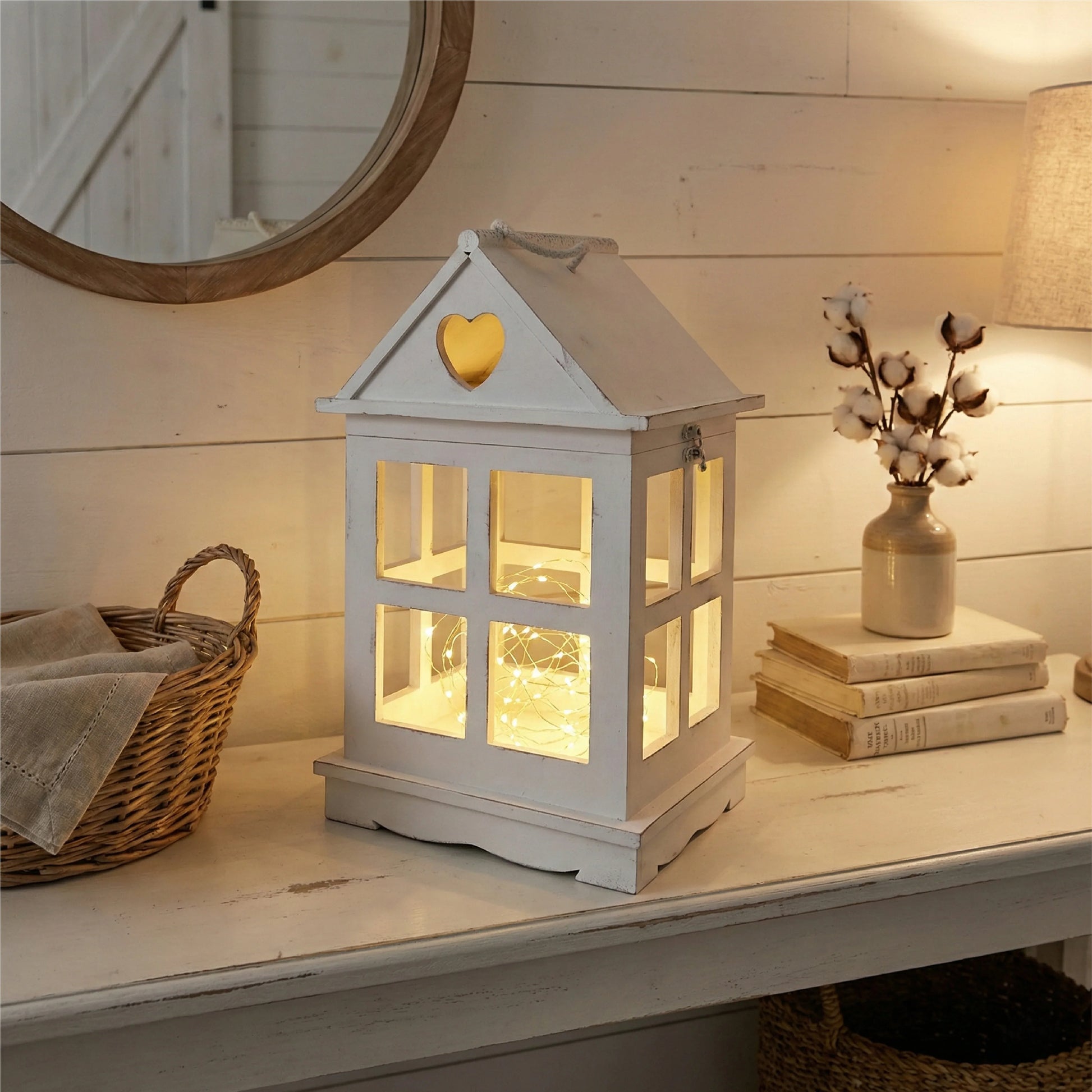 White lantern with heart-shaped window on a wooden surface with books and a vase.