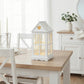 White house-shaped lantern on a wooden table in a bright room with white walls and furniture.