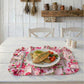 Cooked fish and vegetables on a floral ruffled placemat atop a white wooden table with a rustic wall background.
