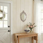 Small ornate mirror on shiplap wall over a console table with a jute runner, roses, lavender, and a white Dutch door.