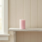 Small pink pillar candle on a white distressed wooden shelf against a cream shiplap wall.