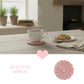 Steaming cup of coffee on a pink coaster with cookies on a plate, set against a cozy indoor background.
