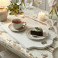 Tea cup with a slice of cake on a rustic wooden table with candles and flowers.