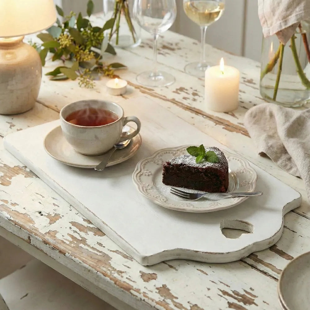 Tea cup with a slice of cake on a rustic wooden table with candles and flowers.