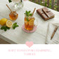 Tea with lemon and mint on a table with a notebook and pen, surrounded by lemons and mint leaves.