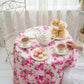Tea party setup with tea set, pastries, and cookies on a floral tablecloth.