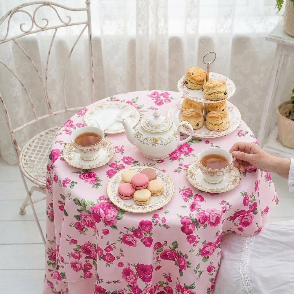 Tea party setup with tea set, pastries, and cookies on a floral tablecloth.