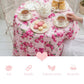 Tea set on a floral tablecloth with tea cups, teapot, and pastries.