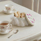 Tea set with floral teacups and cookies in a decorative tin on a white table.