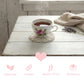 Teacup with floral design on a pink woven coaster on a wooden table, with lavender and a heart symbol.
