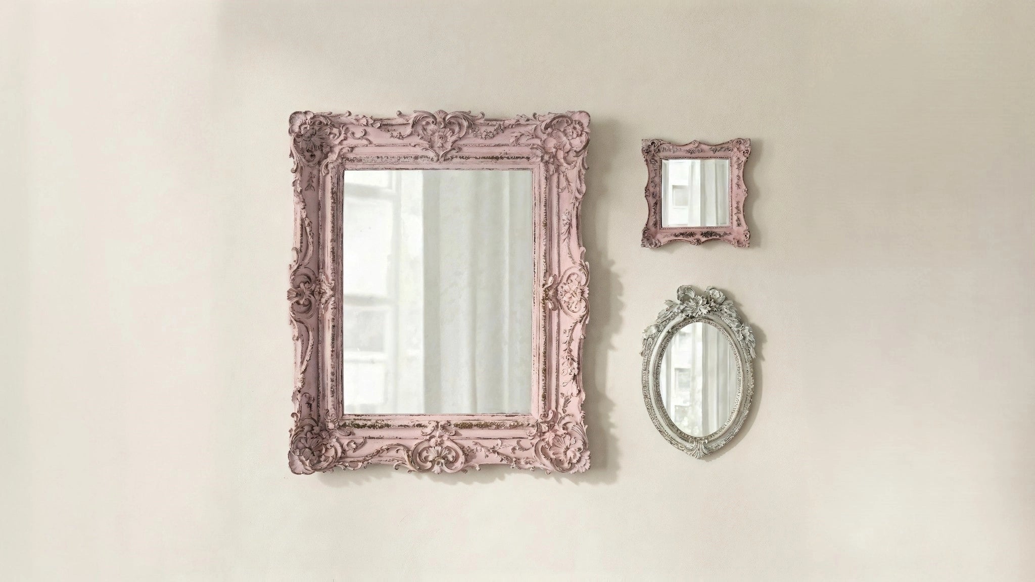 Three decorative mirrors with ornate pink frames on a beige wall.