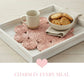 Tray with pink woven mat, white mug, and bowl of cookies on a light wooden surface.