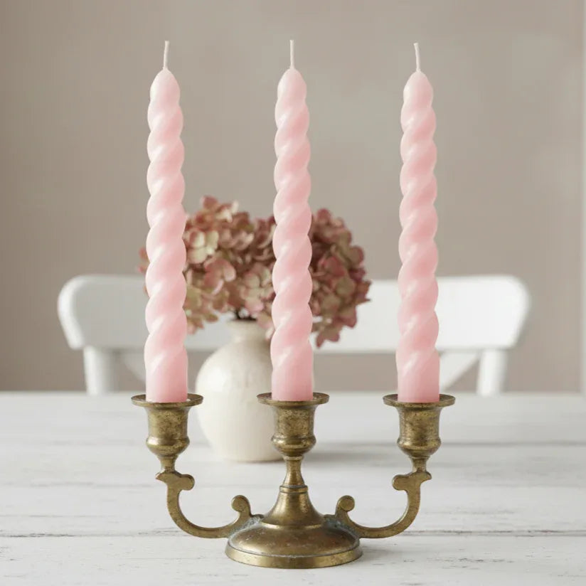 Three pink twisted candles in a brass candle holder on a neutral background