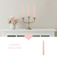 Decorative setup with pink candles, a vase of flowers, and a candelabra on a white surface.