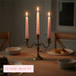 Candle holder with pink candles on a dining table with food and cutlery.