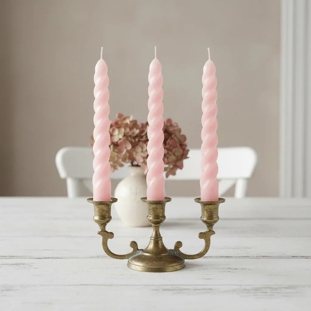 Three pink twisted candles in a brass candlestick holder on a wooden surface with a blurred background.