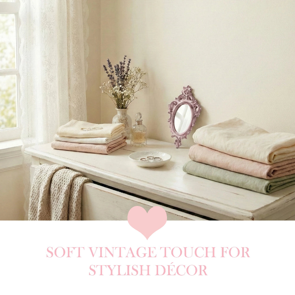 Folded blankets, lavender vase, and an ornate purple mirror on a white dresser with pink text below.