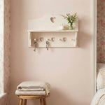 Wall-mounted shelf with heart-shaped hooks and a small plant in a bedroom setting.