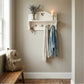 Wall-mounted wooden shelf with hooks, a candle, and a vase against a beige wall. Jackets and keys are hanging on the wall