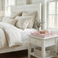 Neatly made bed with white bedding and pillows in a bright bedroom.