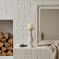 White brick fireplace with stacked firewood, a candle, and a framed mirror.