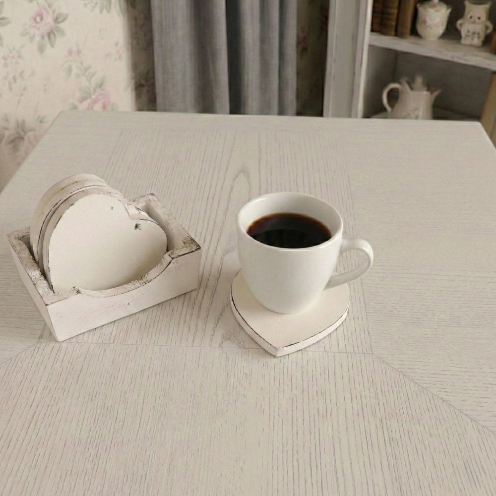 White coffee cup on a heart-shaped coaster next to a matching coaster set on a light wood table with floral wallpaper.